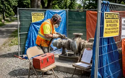Worker sandblasting a pump inside a fenced work area