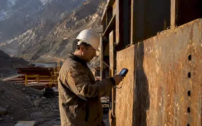 Inspector testing a rusted steel plate at a mountain site