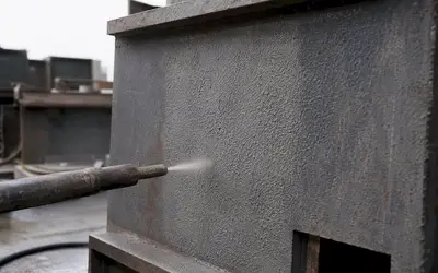 Close-up of a spray gun coating a gray steel box